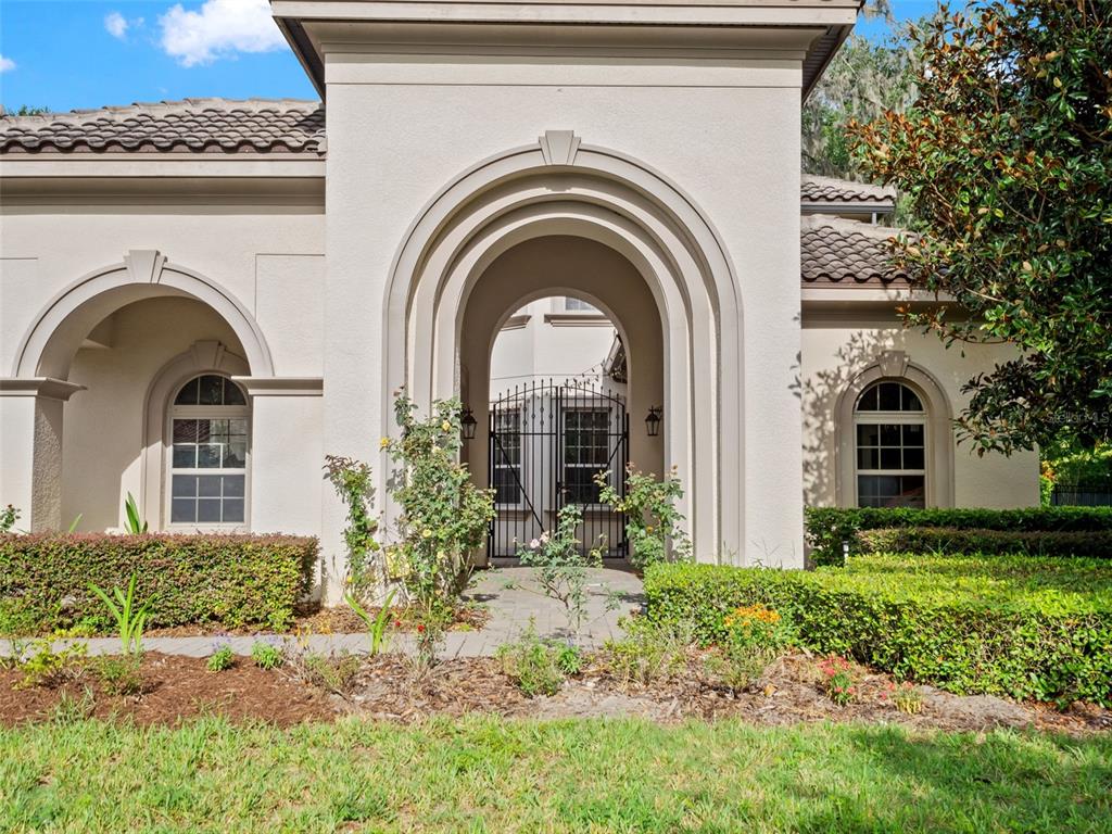 A beige stucco house exterior features a prominent arched entryway with a black metal gate — 7361 BELLA FORESTA PLACE, SANFORD, FL