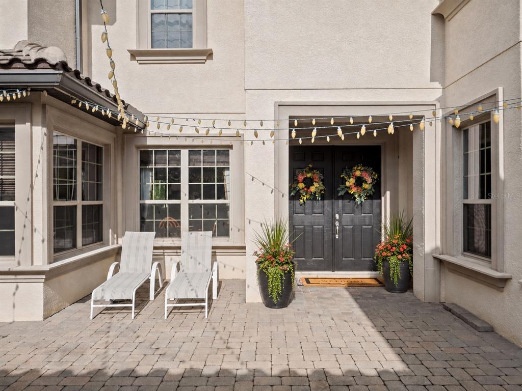 A paved patio features two lounge chairs, potted plants, and string lights before double doors — 7361 BELLA FORESTA PLACE, SANFORD, FL