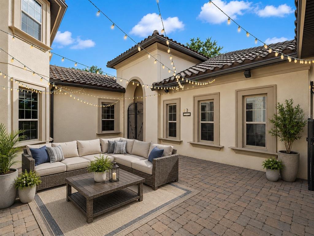 A furnished patio features a sectional sofa, coffee table, and string lights against a stucco house — 7361 BELLA FORESTA PLACE, SANFORD, FL