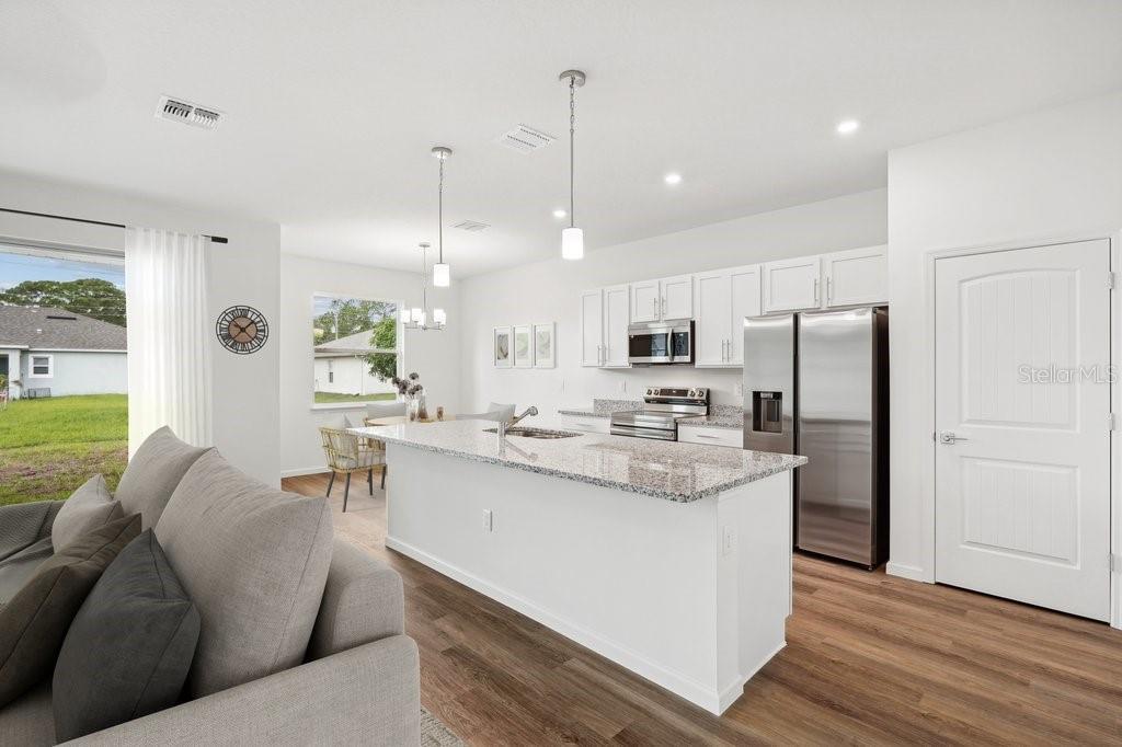 A modern kitchen with white cabinets, granite countertops, and stainless steel appliances overlooks a living area — 7 BUFFALO BILL DRIVE, PALM COAST, FL