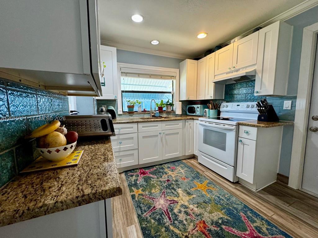 A kitchen features white cabinets, granite countertops, a blue tiled backsplash, and a starfish rug — 324 SW 3rd Ave, Delray Beach FL 33444, DELRAY BEACH, FL
