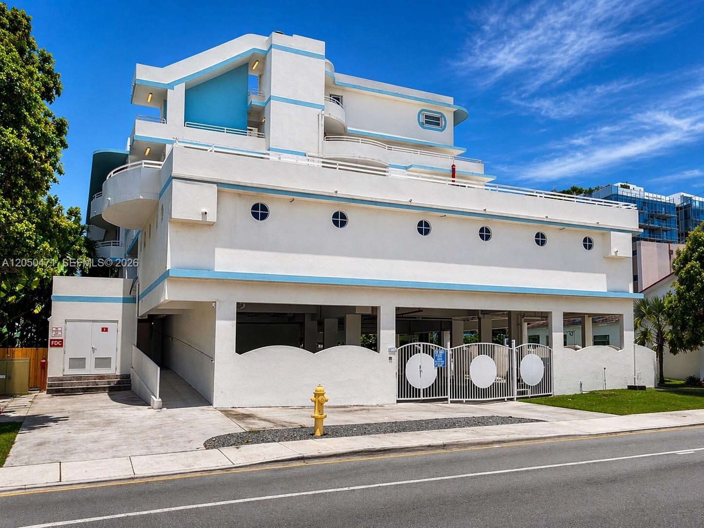 A white multi-story building with blue accents features a ground-level parking garage and porthole windows — 9156 Collins Ave # 107, Surfside FL 33154, SURFSIDE, FL