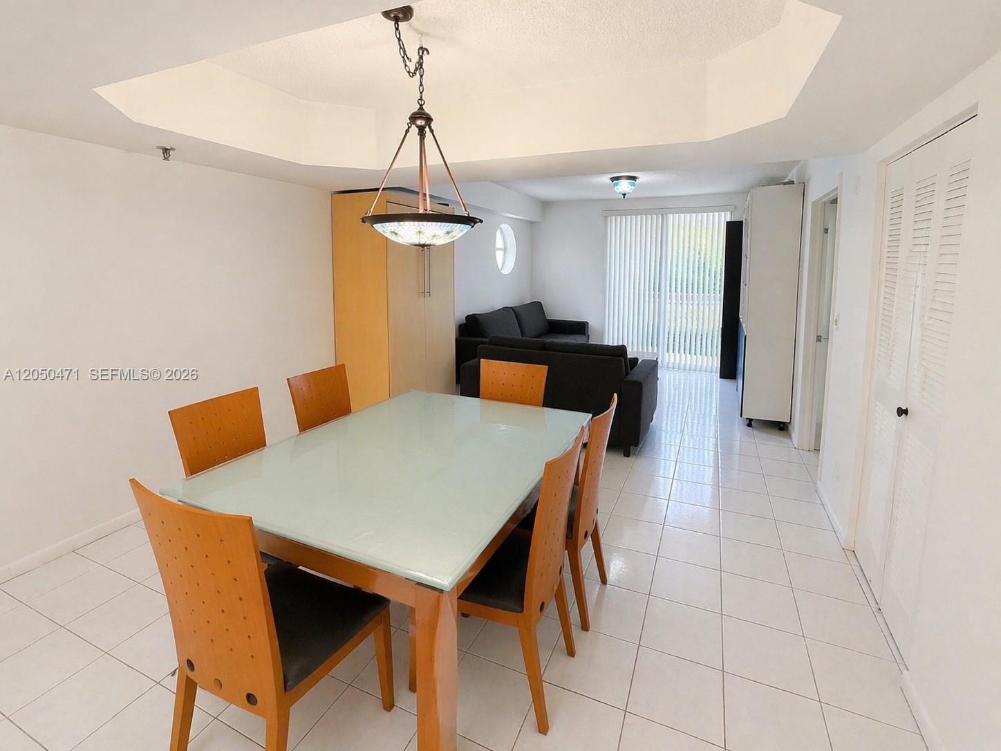 A dining area with a glass-topped table and chairs leads into a living room — 9156 Collins Ave # 107, Surfside FL 33154, SURFSIDE, FL