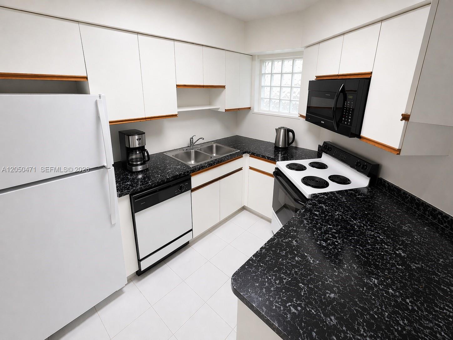 A kitchen features white cabinets, black countertops, white appliances, and a glass block window — 9156 Collins Ave # 107, Surfside FL 33154, SURFSIDE, FL