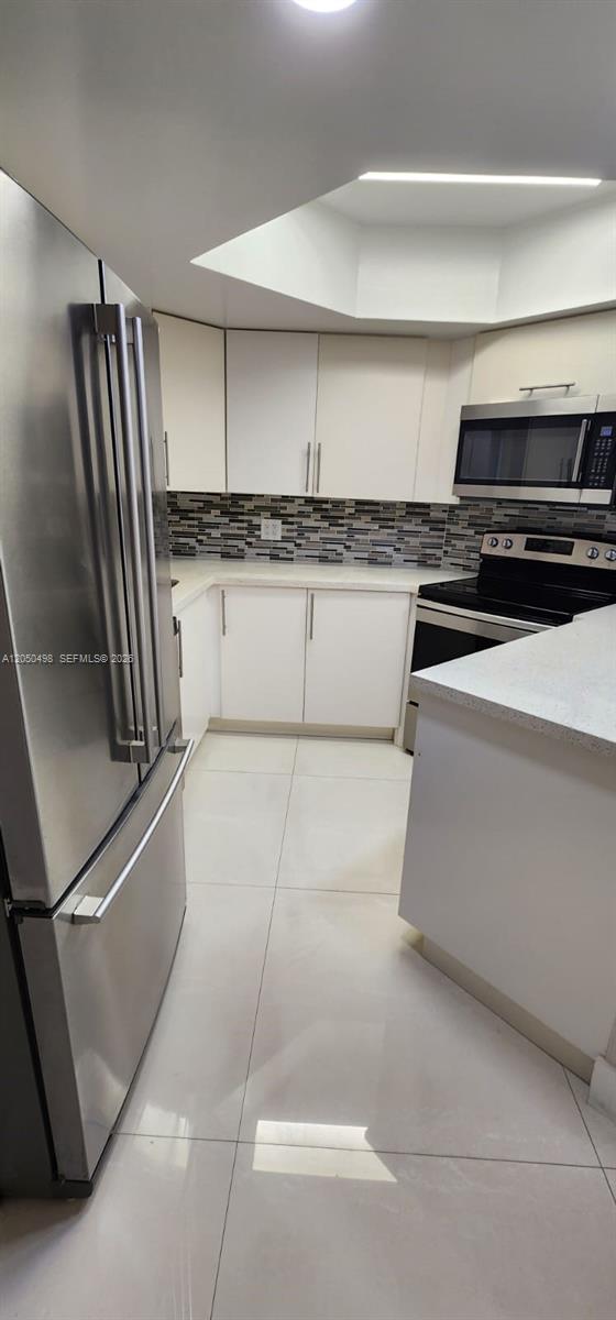 A kitchen features white cabinets, stainless steel appliances, a tiled backsplash, and light-colored floor tiles — 8205 Lake Dr # 101, Doral FL 33166, DORAL, FL