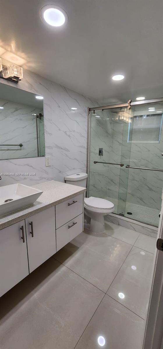A modern bathroom features a white vanity, marble-style wall tiles, and a glass-enclosed shower — 8205 Lake Dr # 101, Doral FL 33166, DORAL, FL