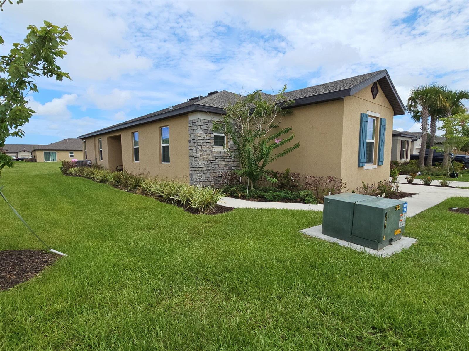 A tan stucco house with stone accents and blue shutters sits on a grassy lot — 1812 Celebration Drive, Fort Pierce FL 34947, FORT PIERCE, FL