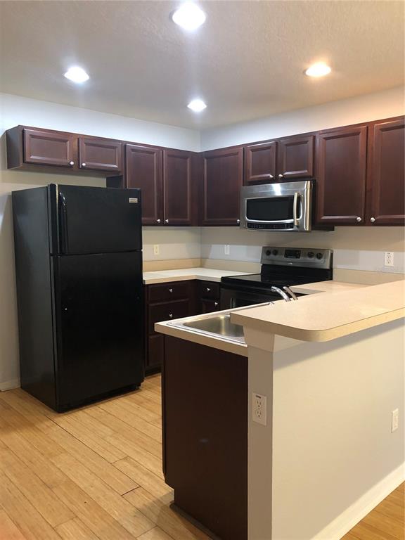 A kitchen features dark wood cabinets, black appliances, light countertops, and light wood flooring — 13442 APPLEROSE LANE UNIT 66, ORLANDO, FL