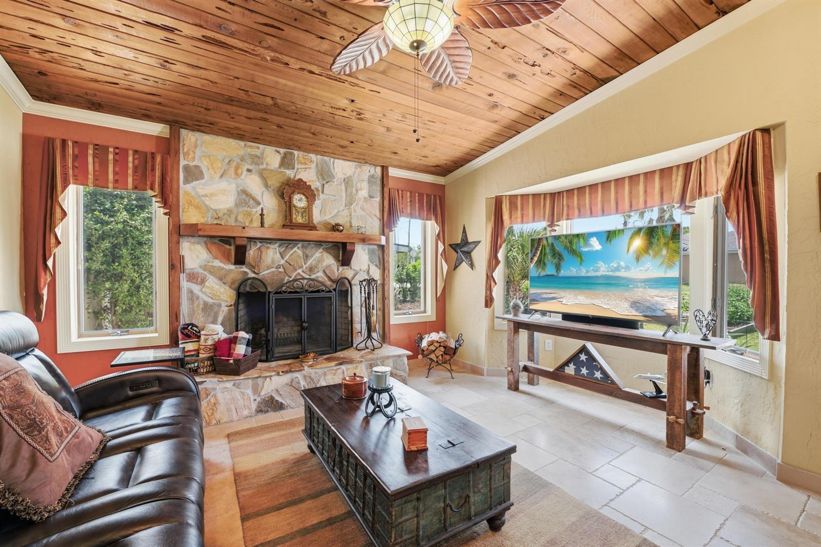 A living room features a stone fireplace, wood-plank ceiling, tile floors, and a television console — 1055 S Brevard Avenue, Cocoa Beach FL 32931, COCOA BEACH, FL