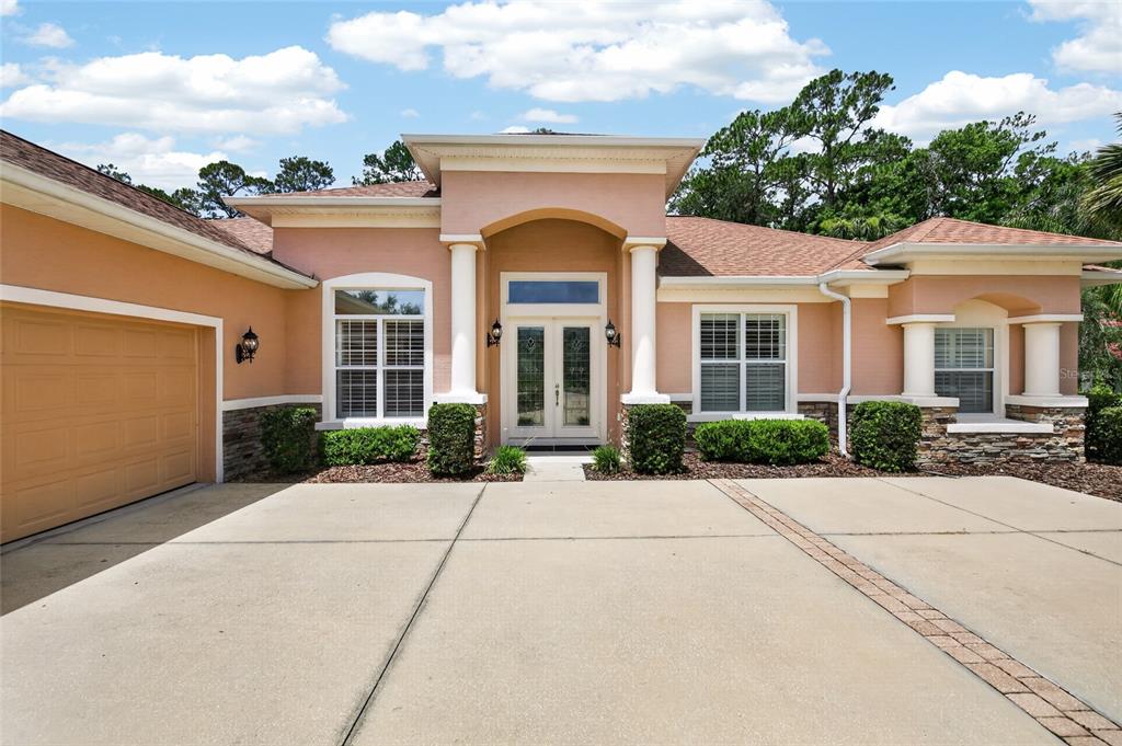 A single-story house with a peach stucco exterior, stone accents, and a concrete driveway — 6 SCARLET OAK CIRCLE, PALM COAST, FL