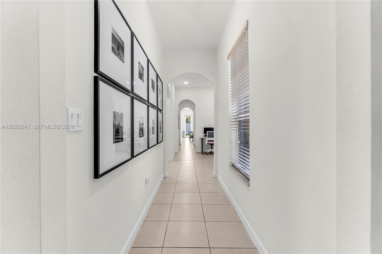 A long hallway features light tile flooring, white walls, a window with blinds, and framed artwork — 17064 SW 90th Way, Miami FL 33196, MIAMI, FL