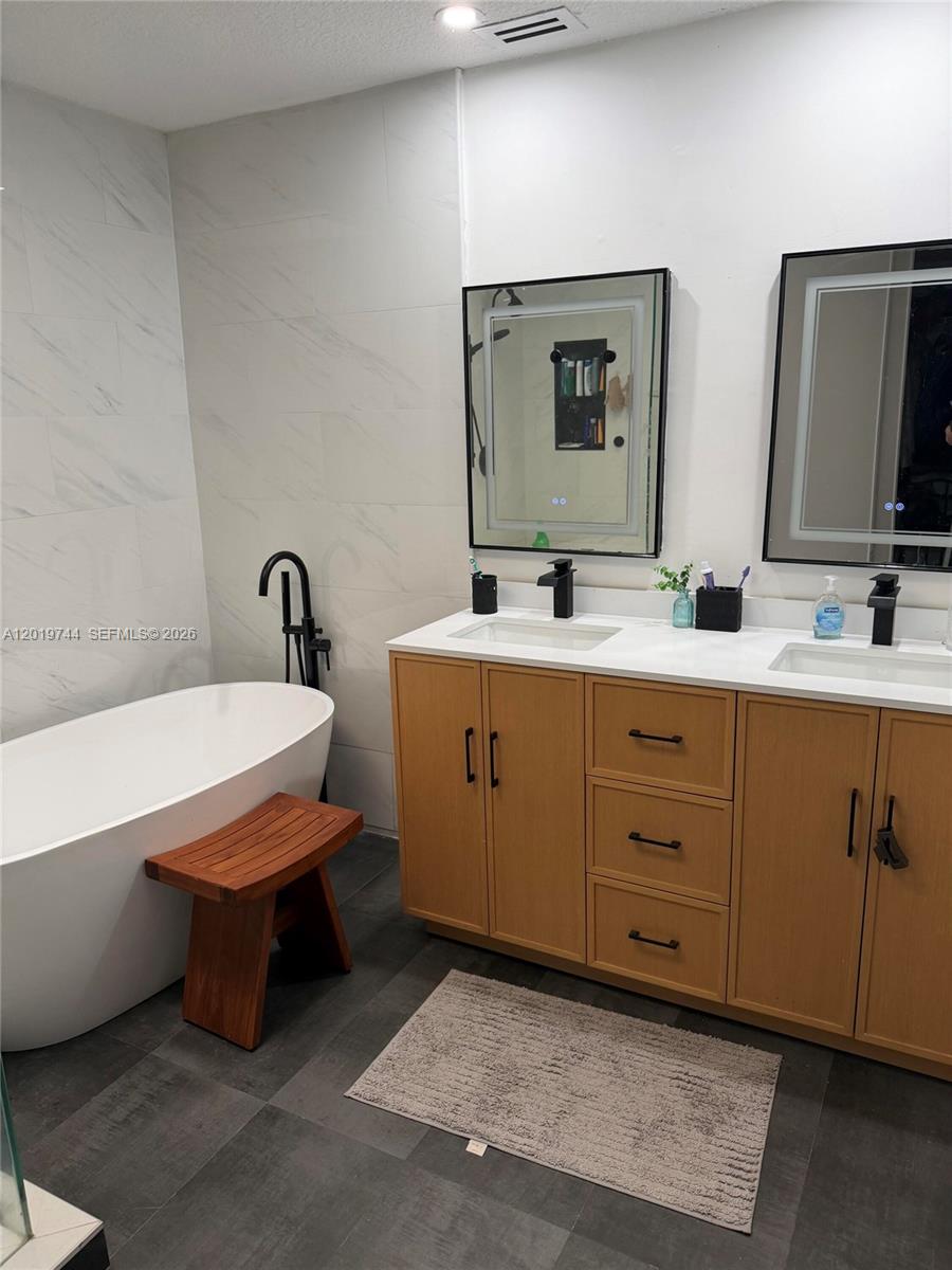 A modern bathroom features a freestanding tub, double vanity with light wood cabinets, and mirrors — 1481 NW 104th Ave, Plantation FL 33322, PLANTATION, FL