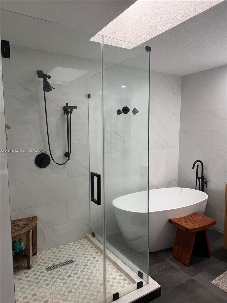 A modern bathroom features a glass-enclosed shower, a freestanding tub, and marble-look wall tiles — 1481 NW 104th Ave, Plantation FL 33322, PLANTATION, FL