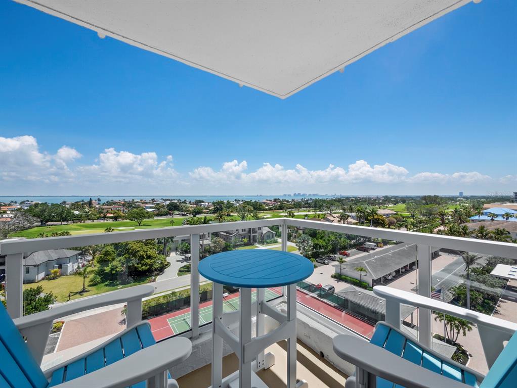 A balcony with a blue table and chairs overlooks a golf course and the ocean — 1050 LONGBOAT CLUB ROAD UNIT 903, LONGBOAT KEY, FL