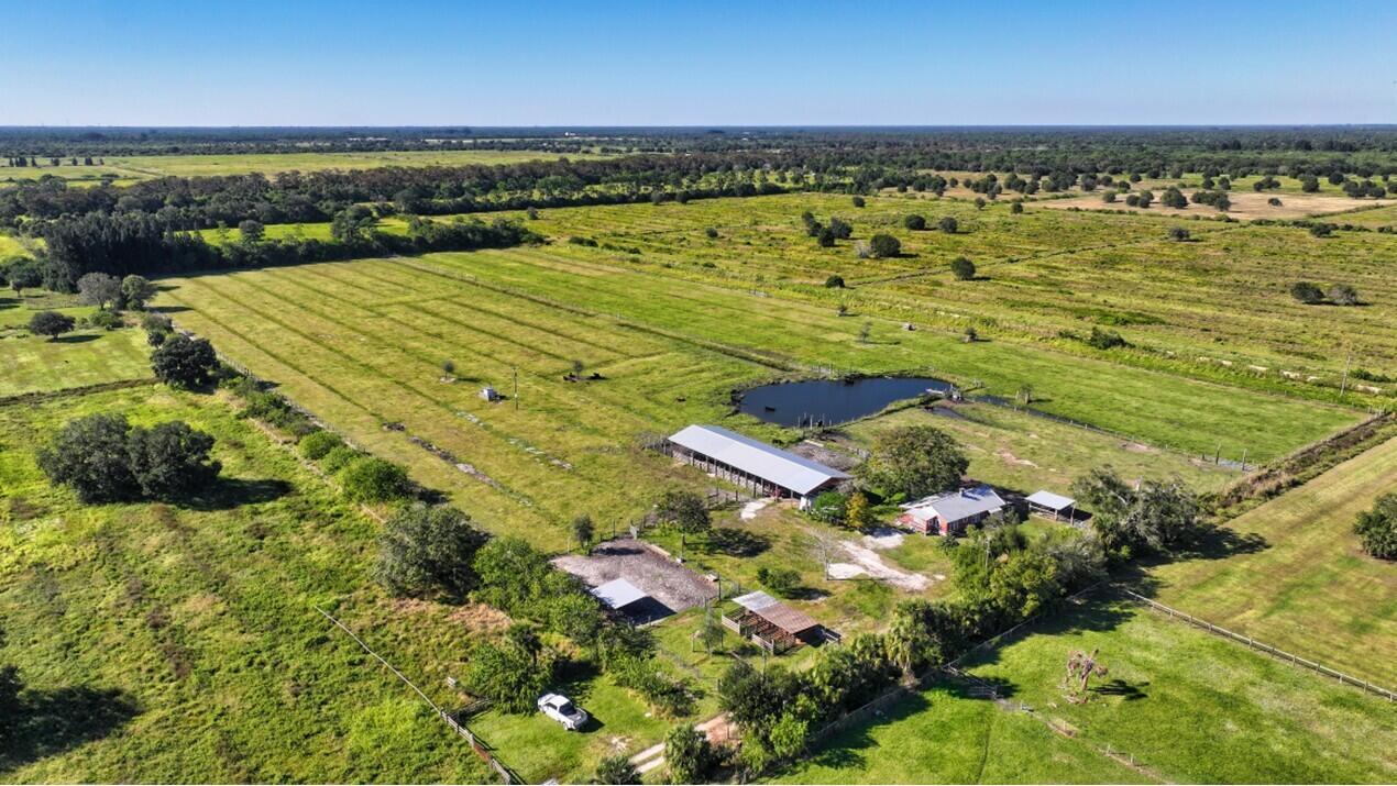 An aerial view of a rural property featuring a house, barn, pond, and fenced pastures — 7230 77th Street, Vero Beach FL 32967, VERO BEACH, FL