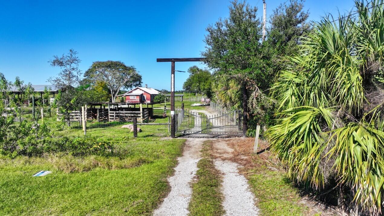 A gravel driveway leads to a gated entrance with a small house and barn beyond — 7230 77th Street, Vero Beach FL 32967, VERO BEACH, FL