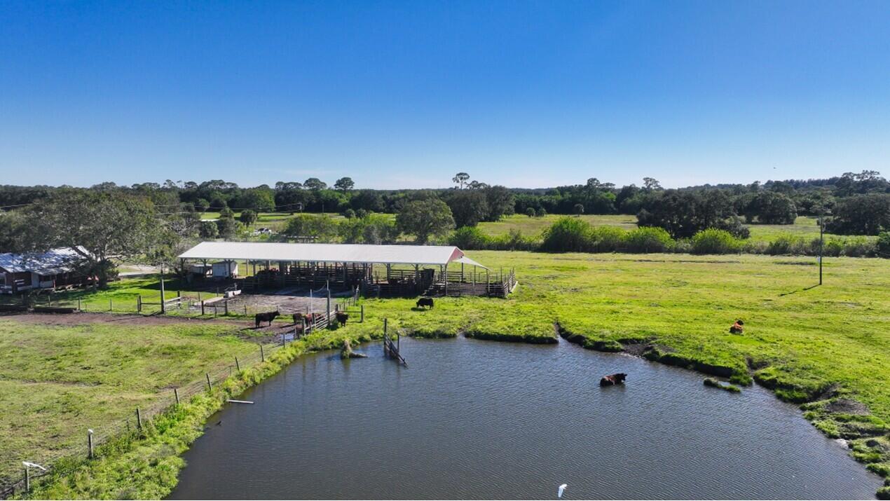 An aerial view of a rural property featuring a cattle barn, pasture, and a pond — 7230 77th Street, Vero Beach FL 32967, VERO BEACH, FL