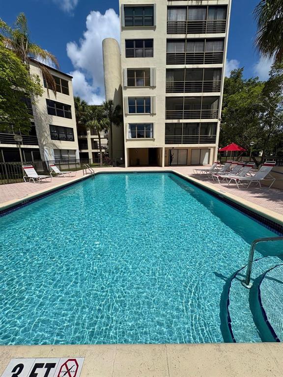 A rectangular swimming pool sits in front of a multi-story apartment building with balconies — 2314 S Cypress Bend Drive Unit 614, Pompano Beach FL 33069, POMPANO BEACH, FL
