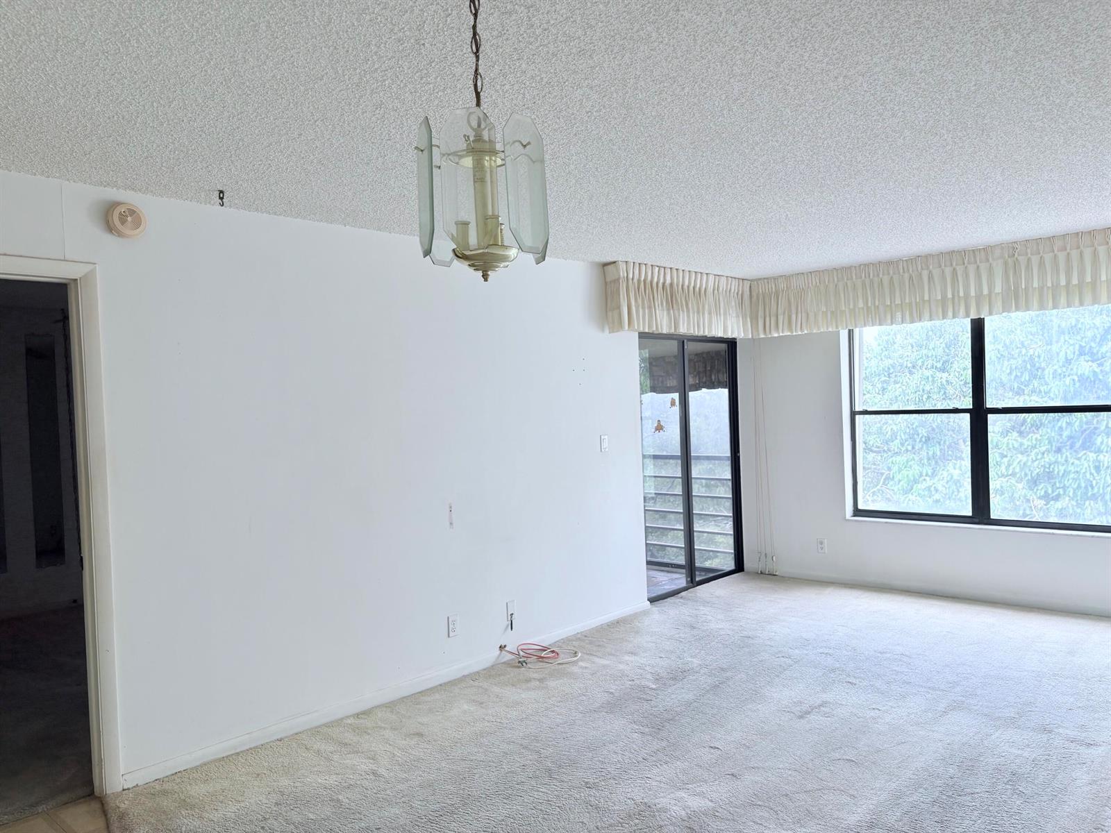 An empty living room features beige carpet, white walls, a textured ceiling, and a glass chandelier — 2314 S Cypress Bend Drive Unit 614, Pompano Beach FL 33069, POMPANO BEACH, FL