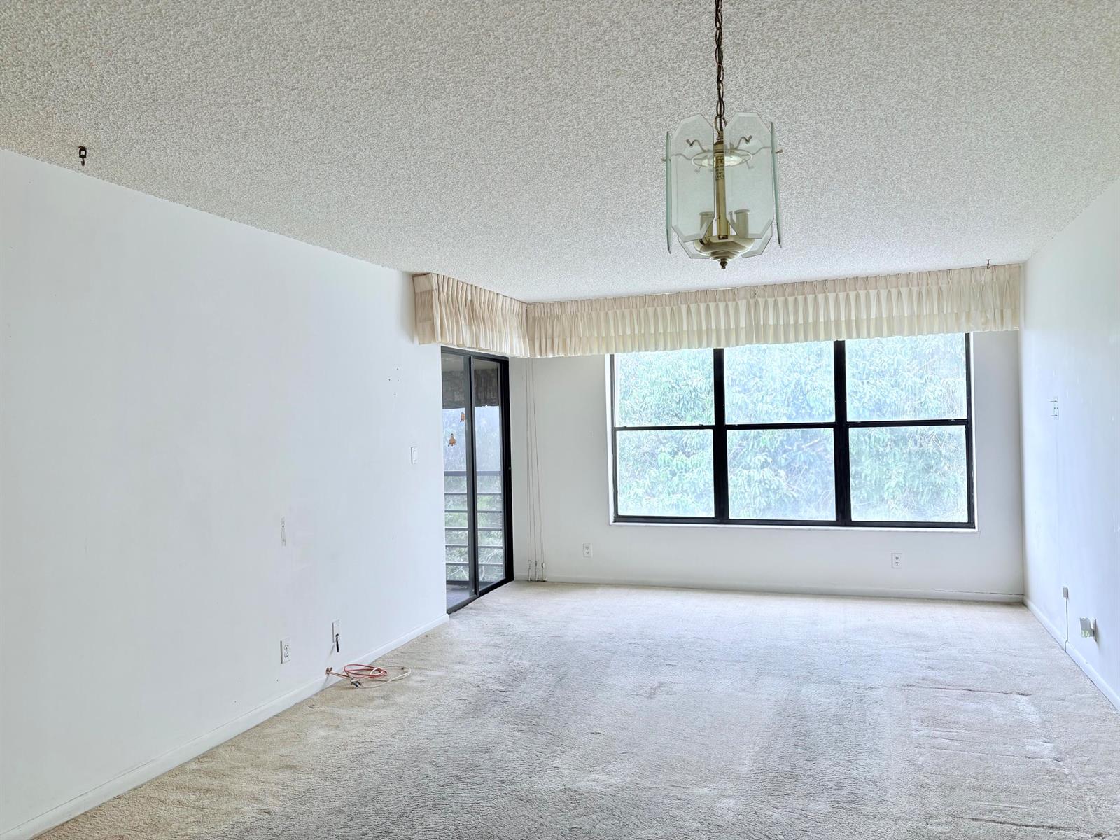 An empty living room features beige carpeting, white walls, a popcorn ceiling, and large windows — 2314 S Cypress Bend Drive Unit 614, Pompano Beach FL 33069, POMPANO BEACH, FL