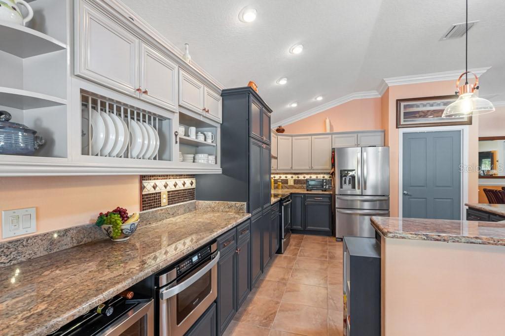 A kitchen features two-toned cabinetry, granite countertops, stainless steel appliances, and light-colored tile flooring — 2611 JUPITER WAY, THE VILLAGES, FL