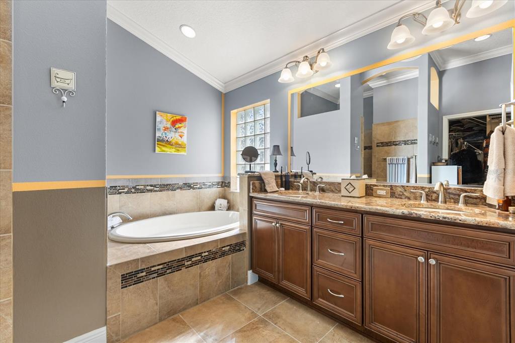 A bathroom features a soaking tub, double vanity with granite countertops, and glass block windows — 2611 JUPITER WAY, THE VILLAGES, FL