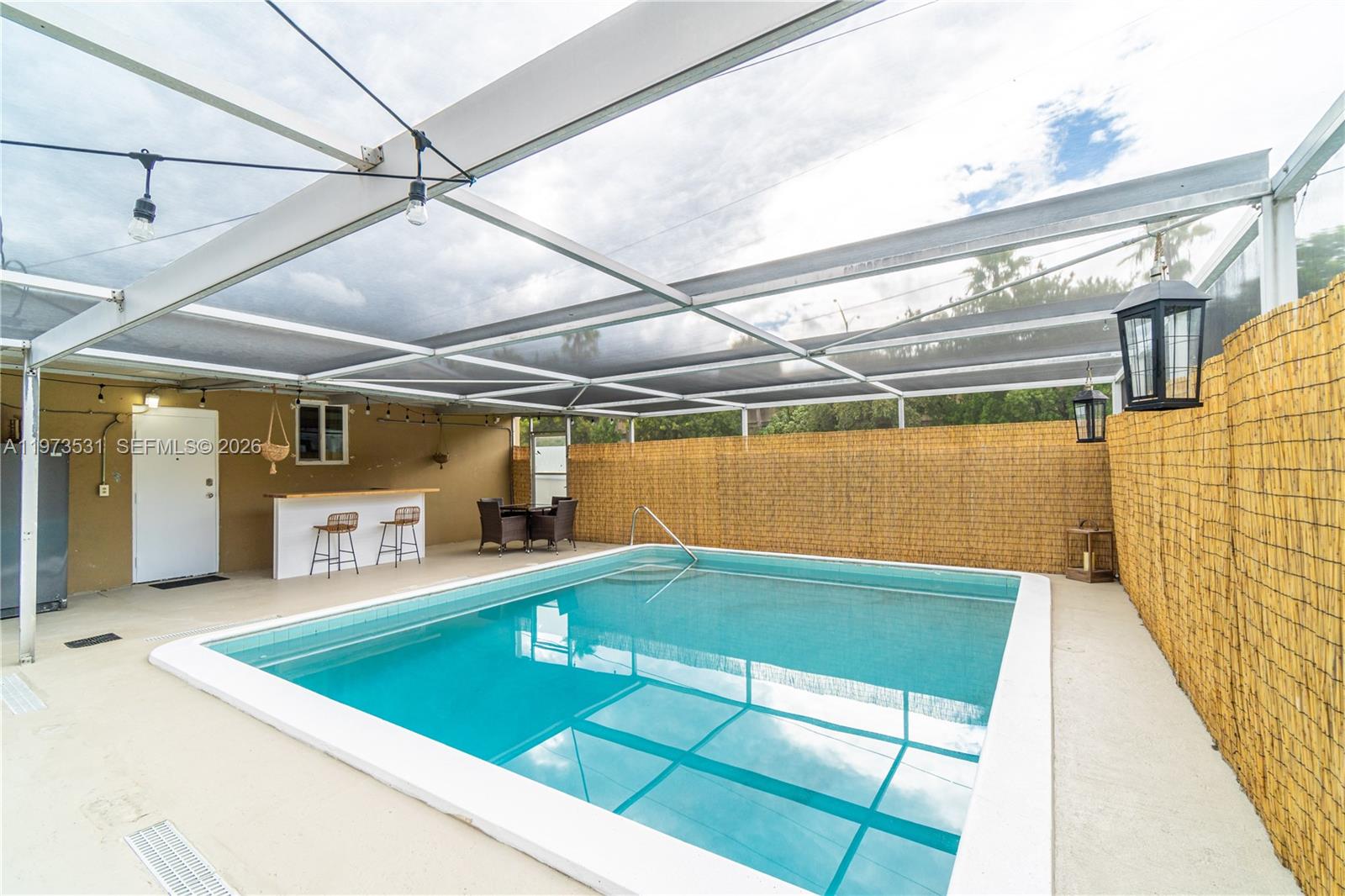A rectangular swimming pool is enclosed by a screened lanai with a bamboo privacy fence — 13405 NW 6th Ave, North Miami FL 33168, NORTH MIAMI, FL