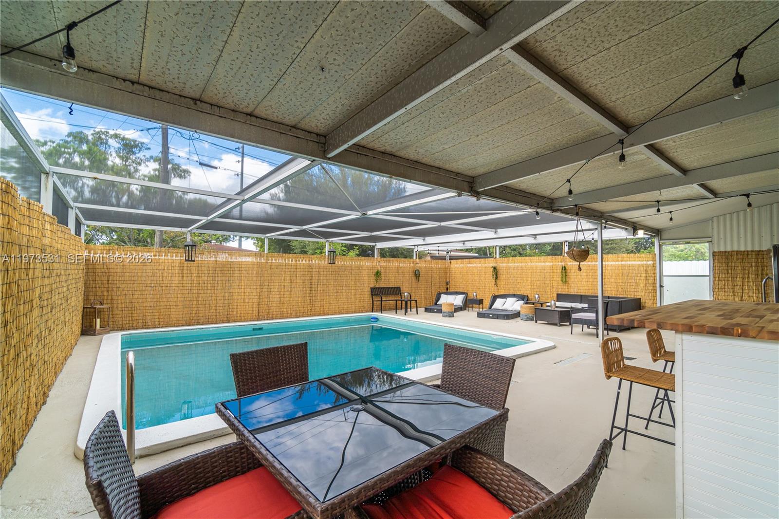 A covered patio features a swimming pool, outdoor furniture, and a bamboo privacy fence — 13405 NW 6th Ave, North Miami FL 33168, NORTH MIAMI, FL