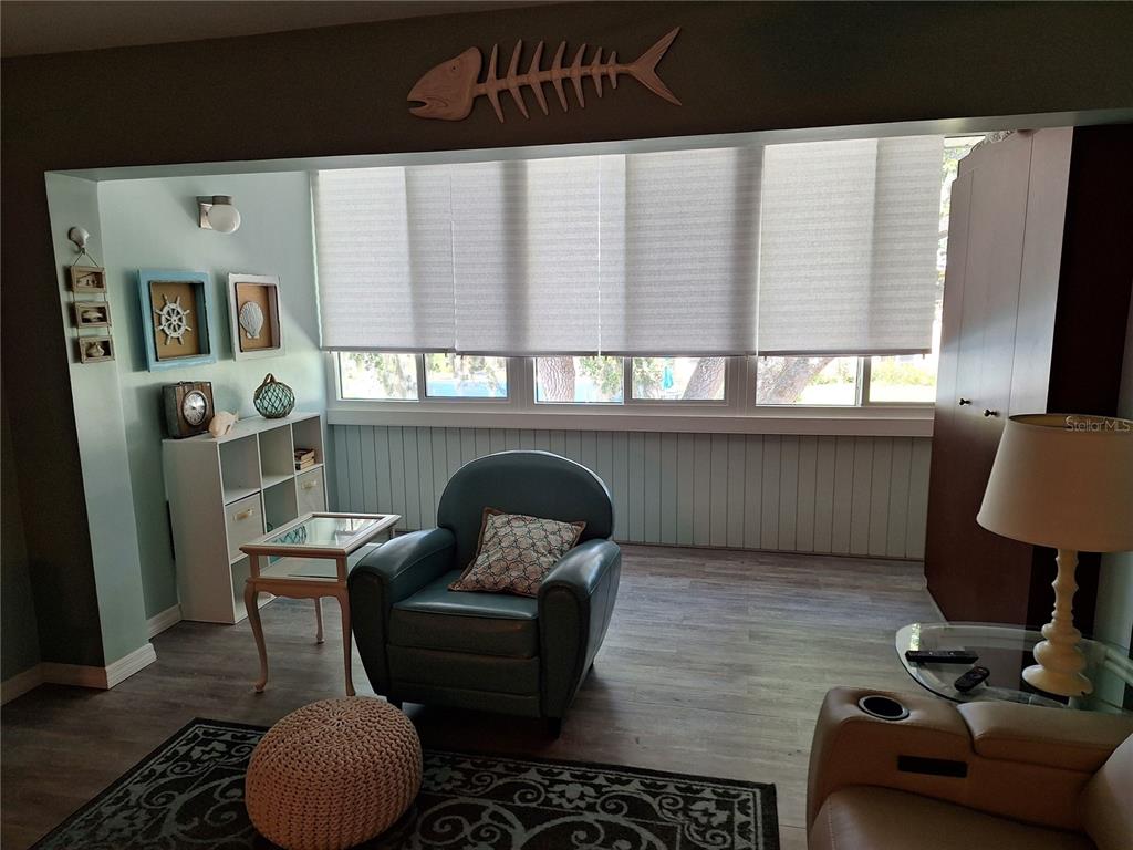 A sunroom features a blue armchair, a white shelving unit, and a wooden fish wall decoration — 2437 HARBOR BOULEVARD UNIT 202, PORT CHARLOTTE, FL