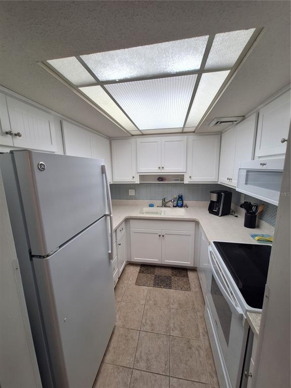 A galley kitchen features white cabinets, light countertops, a tiled backsplash, and a skylight — 2437 HARBOR BOULEVARD UNIT 202, PORT CHARLOTTE, FL