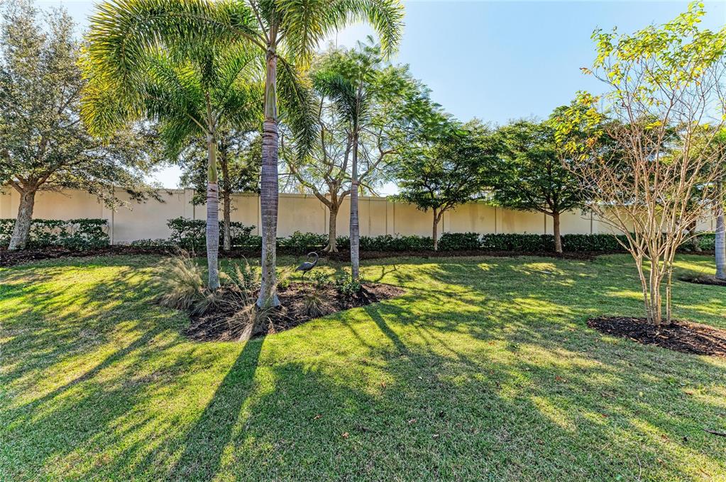 A grassy backyard features palm trees, mature landscaping, and a tall privacy wall — 131 MARAVIYA BOULEVARD, NOKOMIS, FL