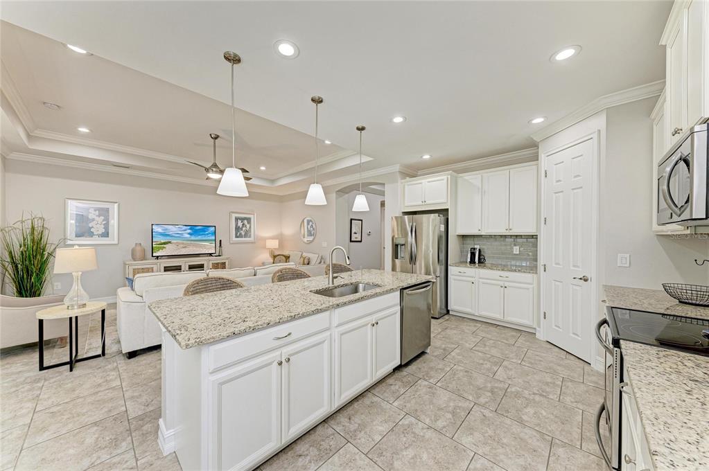 A kitchen with white cabinets, granite countertops, and an island opens into a living area — 131 MARAVIYA BOULEVARD, NOKOMIS, FL