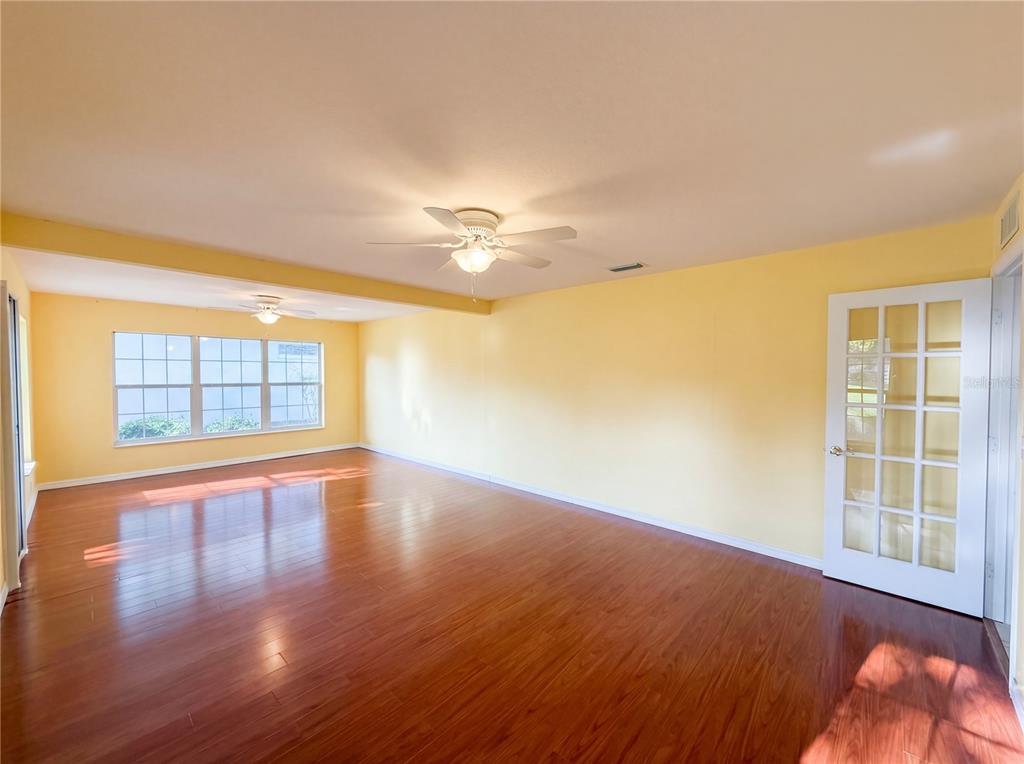 An empty room with yellow walls, wood-look flooring, two ceiling fans, and a glass-paneled door — 7319 SW 115TH PLACE, OCALA, FL