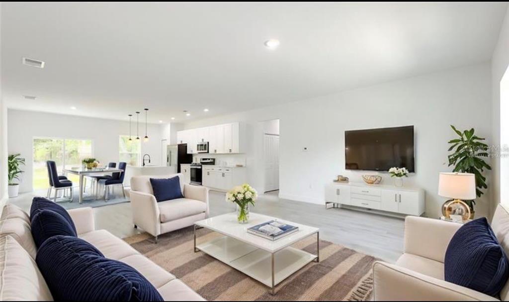 A bright, open-concept living room and kitchen featuring white cabinetry, light flooring, and modern furniture — 5669 N CLAREMONT DRIVE, CITRUS SPRINGS, FL