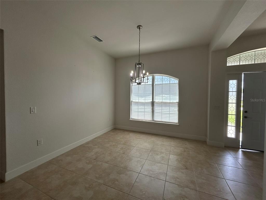 A dining room features tile flooring, a chandelier, and a window with white blinds — 1923 VILLIA STREET, LEHIGH ACRES, FL
