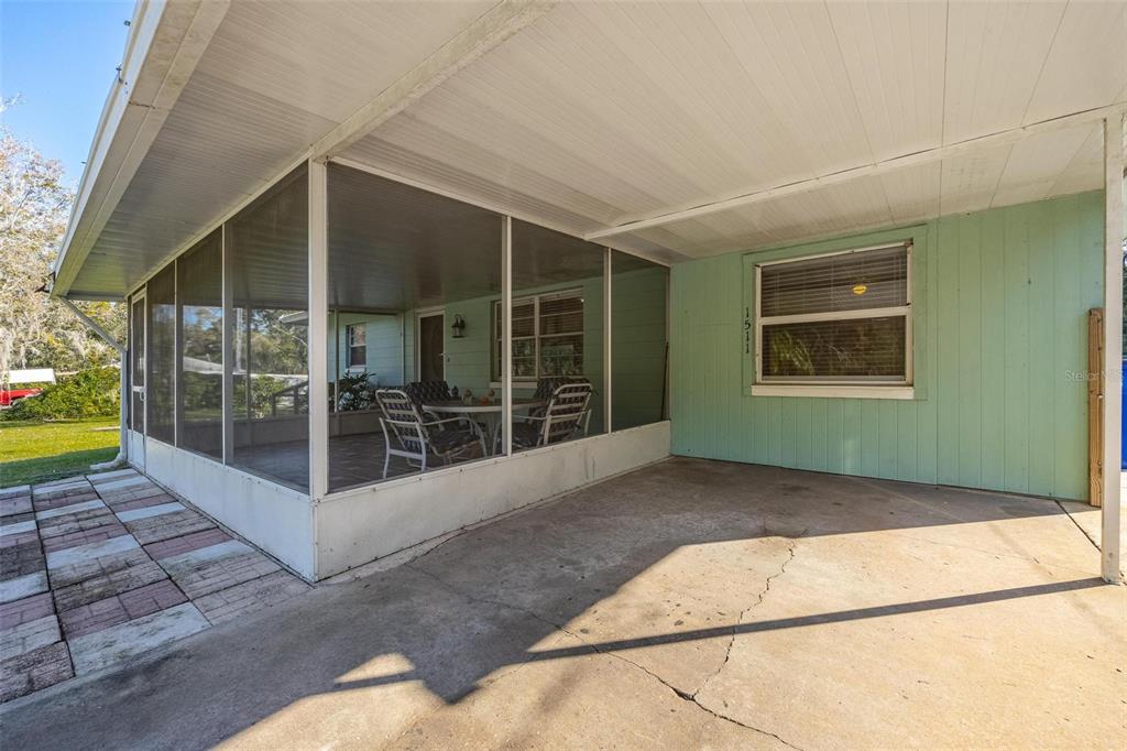 A concrete carport sits beside a screened-in porch with light green siding and a window — 1511 FRINGE STREET, LAKE PLACID, FL
