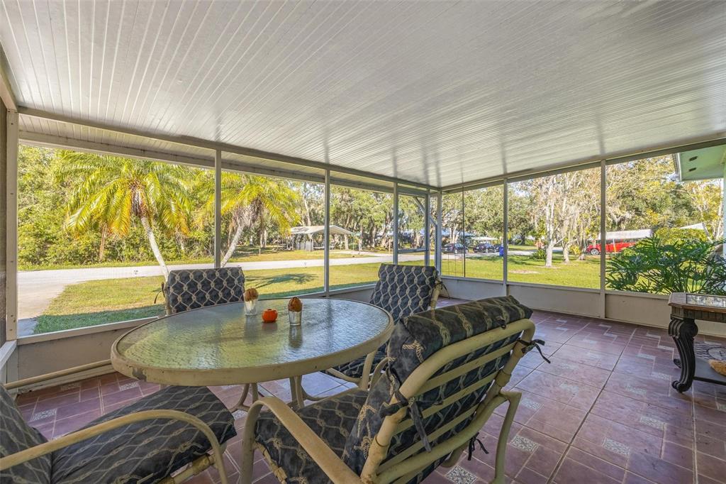 A screened-in porch with a glass-top table, patterned chairs, and tiled flooring overlooking a yard — 1511 FRINGE STREET, LAKE PLACID, FL