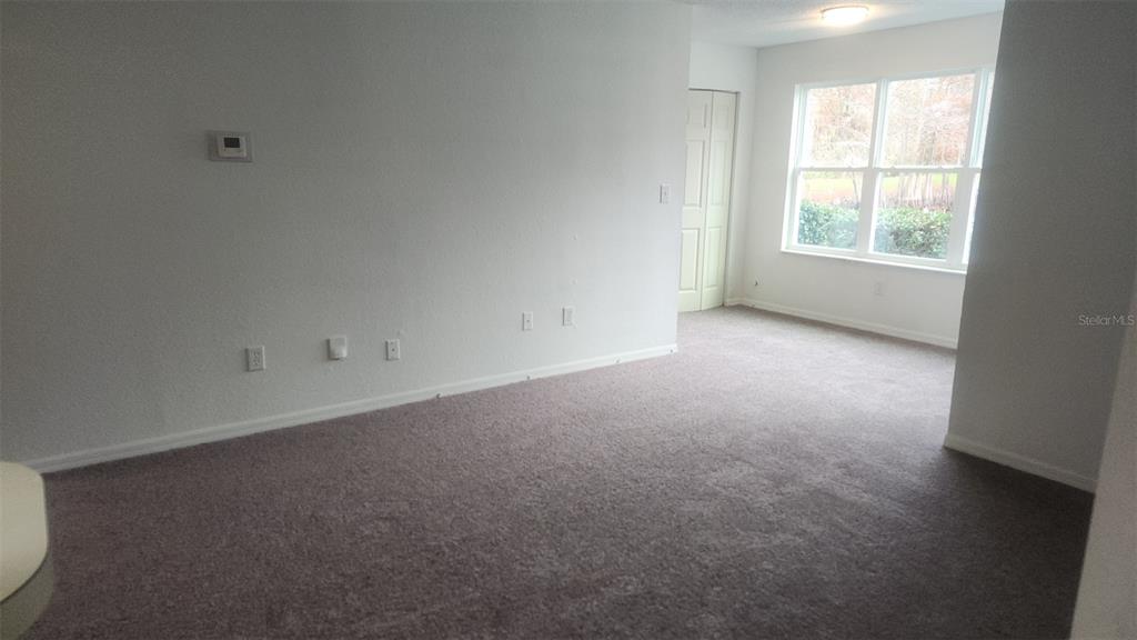 An empty room features gray carpeting, light-colored walls, a window, and a closed closet door — 5713 GATLIN AVENUE UNIT 216, ORLANDO, FL