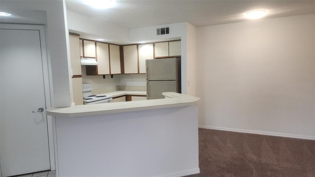 A kitchen with beige cabinets and a breakfast bar overlooks a carpeted living area — 5713 GATLIN AVENUE UNIT 216, ORLANDO, FL