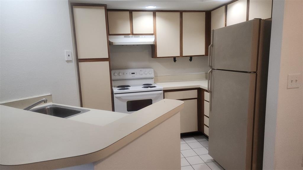 A kitchen features white cabinets, a white stove, a stainless steel refrigerator, and a sink — 5713 GATLIN AVENUE UNIT 216, ORLANDO, FL