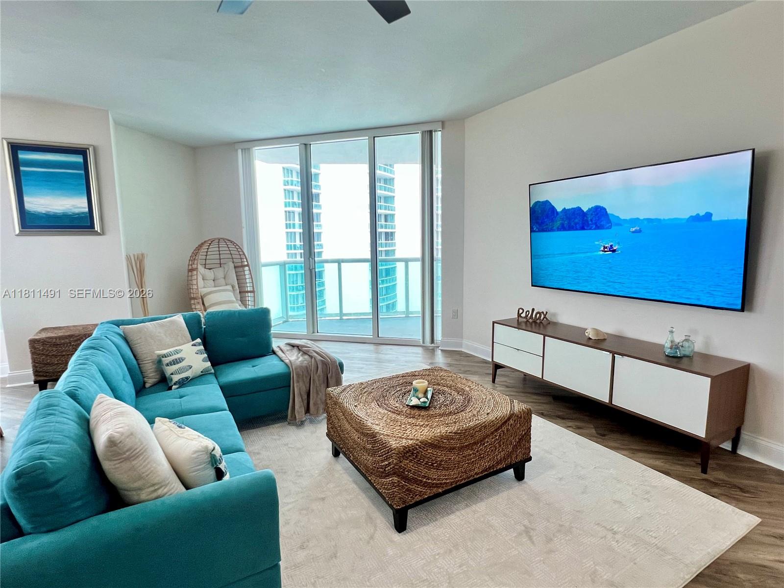 A living room features a teal sectional sofa, a woven ottoman, and a wall-mounted television — 231 Riverside Dr # 1210, Daytona FL 32117, DAYTONA, FL