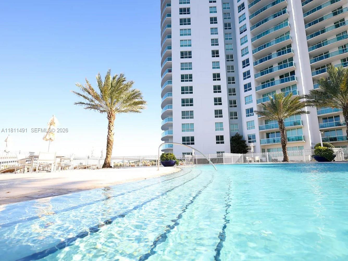 A swimming pool sits in front of a tall white residential building with palm trees — 231 Riverside Dr # 1210, Daytona FL 32117, DAYTONA, FL