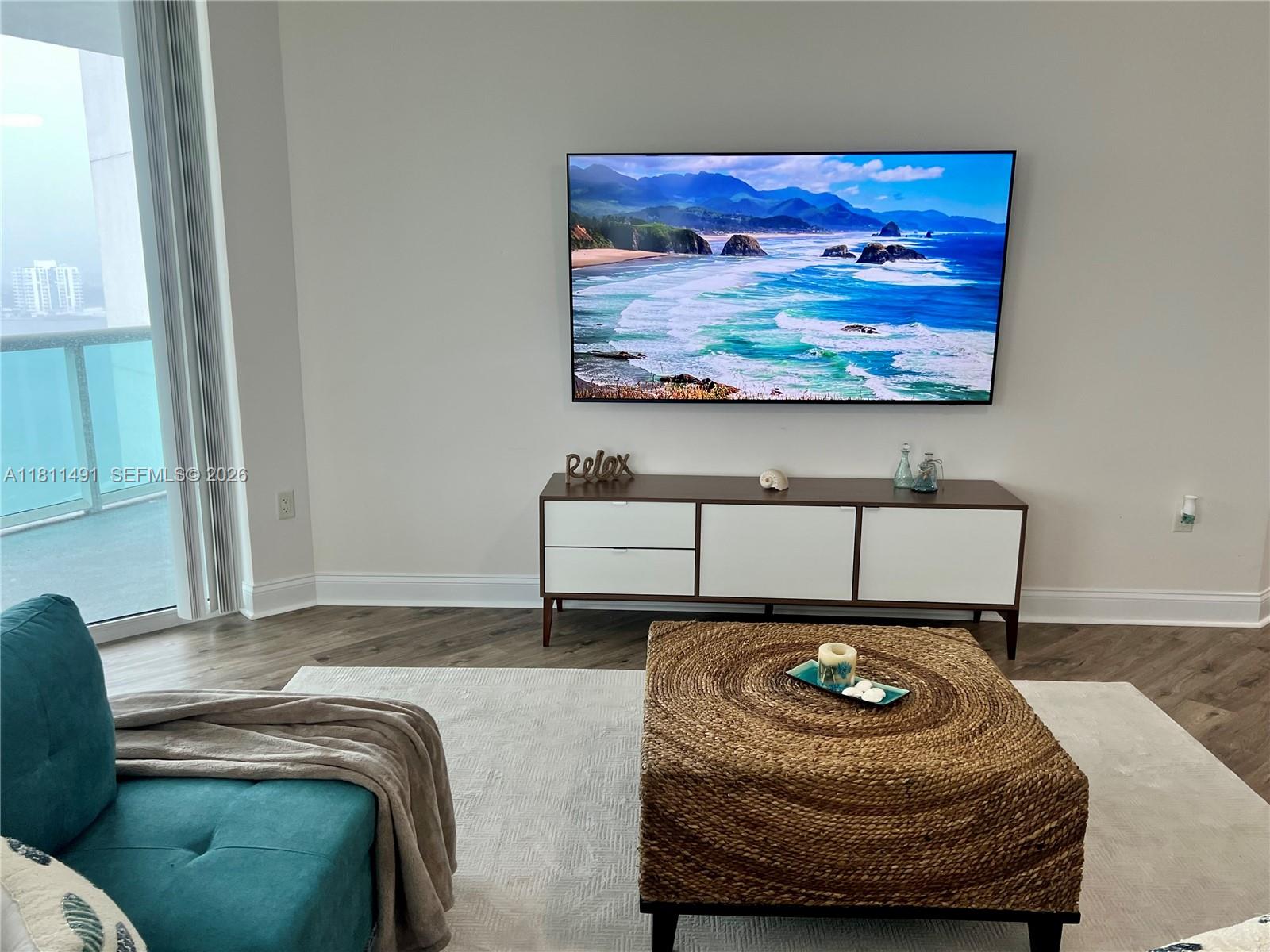 A living room features a wall-mounted television, a media console, and a woven ottoman — 231 Riverside Dr # 1210, Daytona FL 32117, DAYTONA, FL