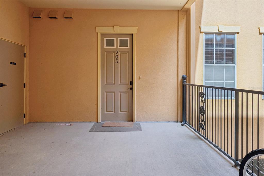 A beige apartment door numbered 205 is located on a concrete balcony with metal railings — 325 NW 14TH STREET UNIT 205, GAINESVILLE, FL