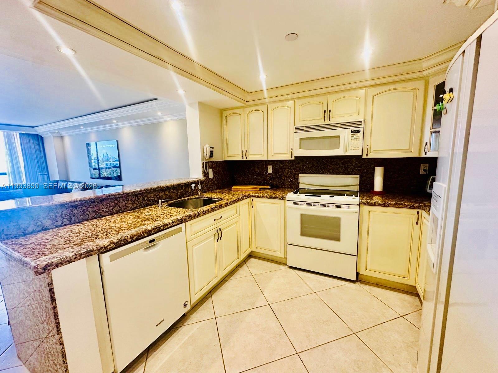 A kitchen features cream-colored cabinets, granite countertops, white appliances, and diagonal floor tiles — 2555 Collins Ave # 704, Miami Beach FL 33140, MIAMI BEACH, FL