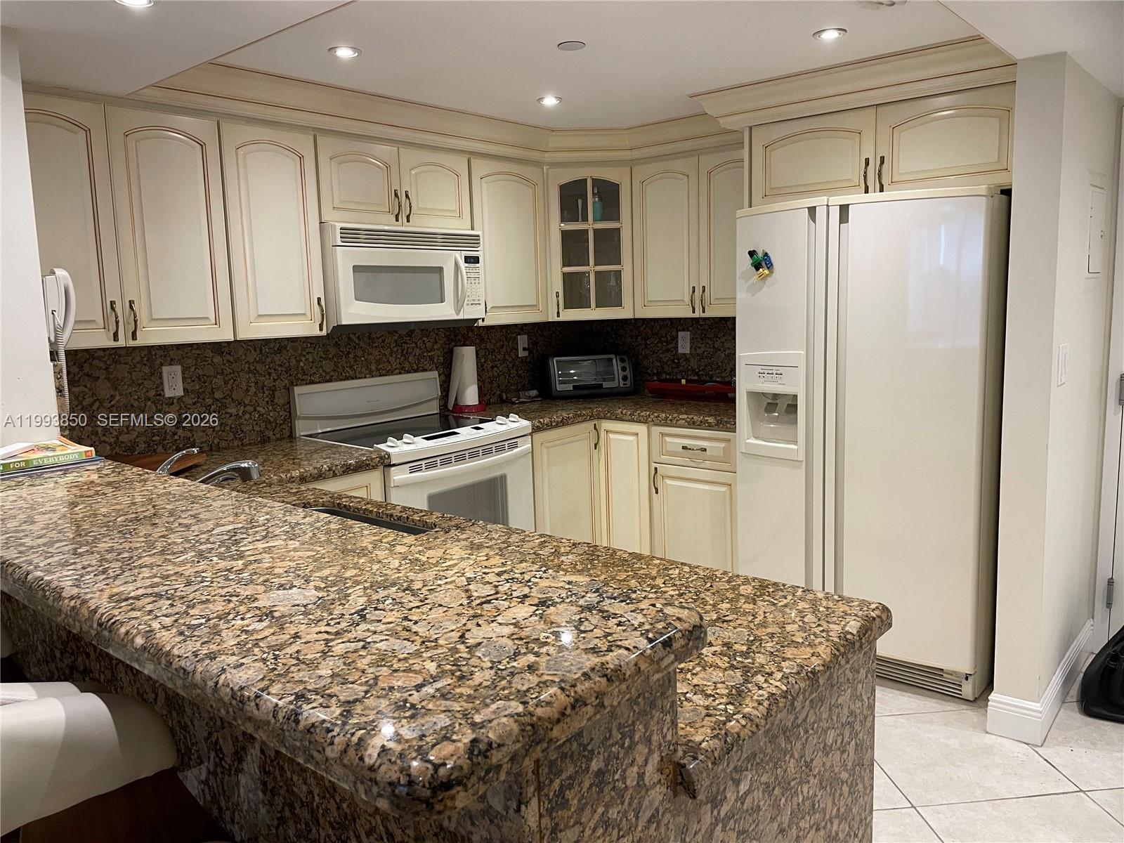 A kitchen features cream-colored cabinets, granite countertops, and white appliances — 2555 Collins Ave # 704, Miami Beach FL 33140, MIAMI BEACH, FL