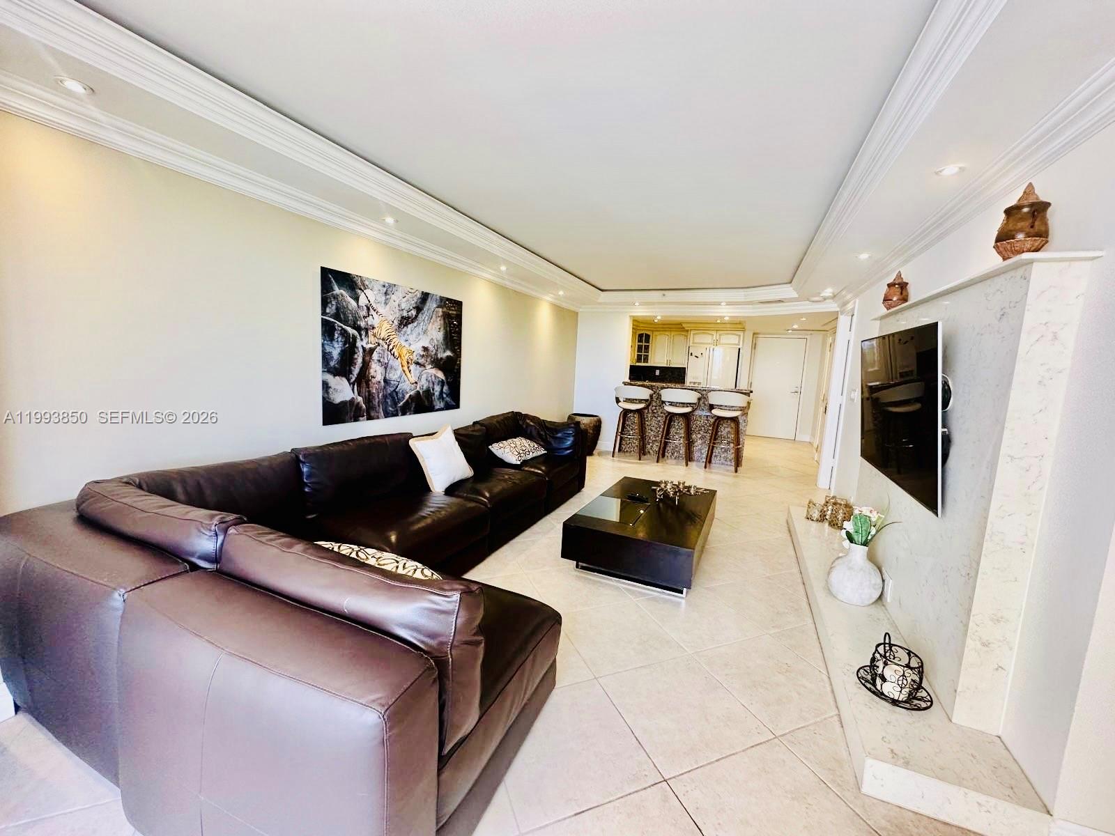 A living room features a large brown sectional sofa, a coffee table, and a kitchen — 2555 Collins Ave # 704, Miami Beach FL 33140, MIAMI BEACH, FL
