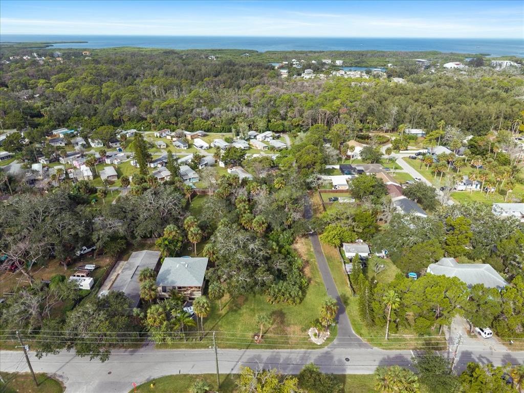 An aerial view shows a residential neighborhood with houses, dense trees, and the ocean beyond — 7601 PIER ROAD, PORT RICHEY, FL