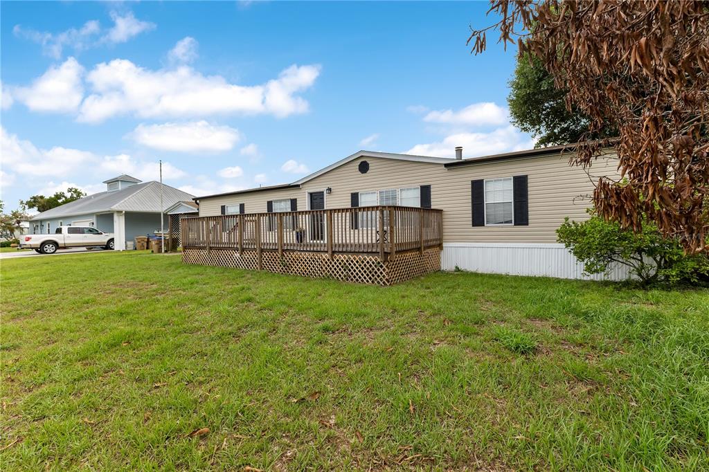A tan mobile home with a wooden deck and lattice skirting sits on a grassy lot — 410 LAGOON COURT, KENANSVILLE, FL