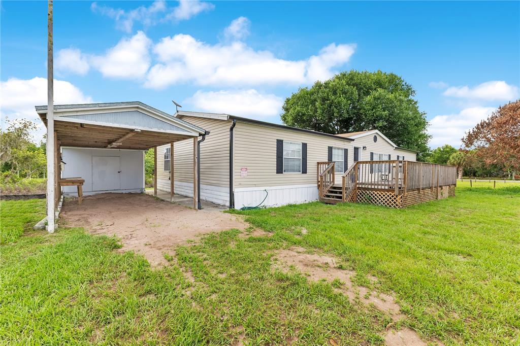 A beige manufactured home features a wooden deck, a carport, and a grassy yard — 410 LAGOON COURT, KENANSVILLE, FL